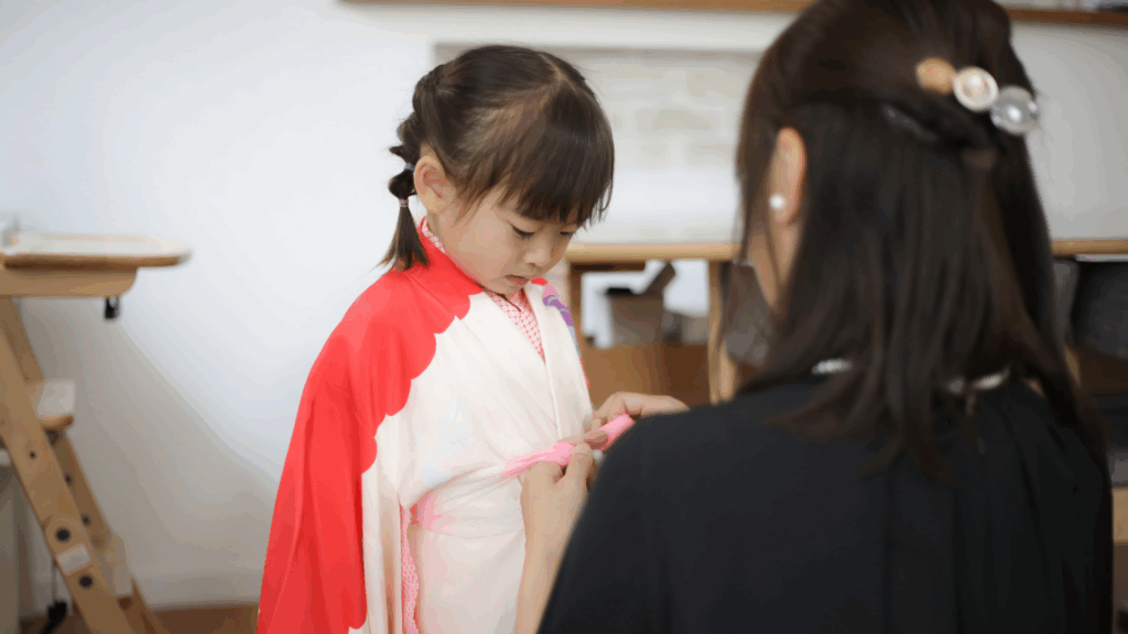 着物を着つけてもらっている女の子